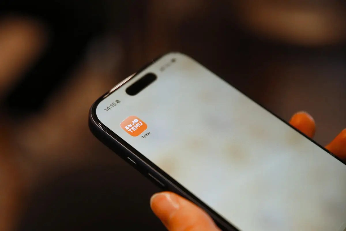 A black iPhone with a white screen showing an orange tinmu app icon for finding deals on trending products at Arba Global