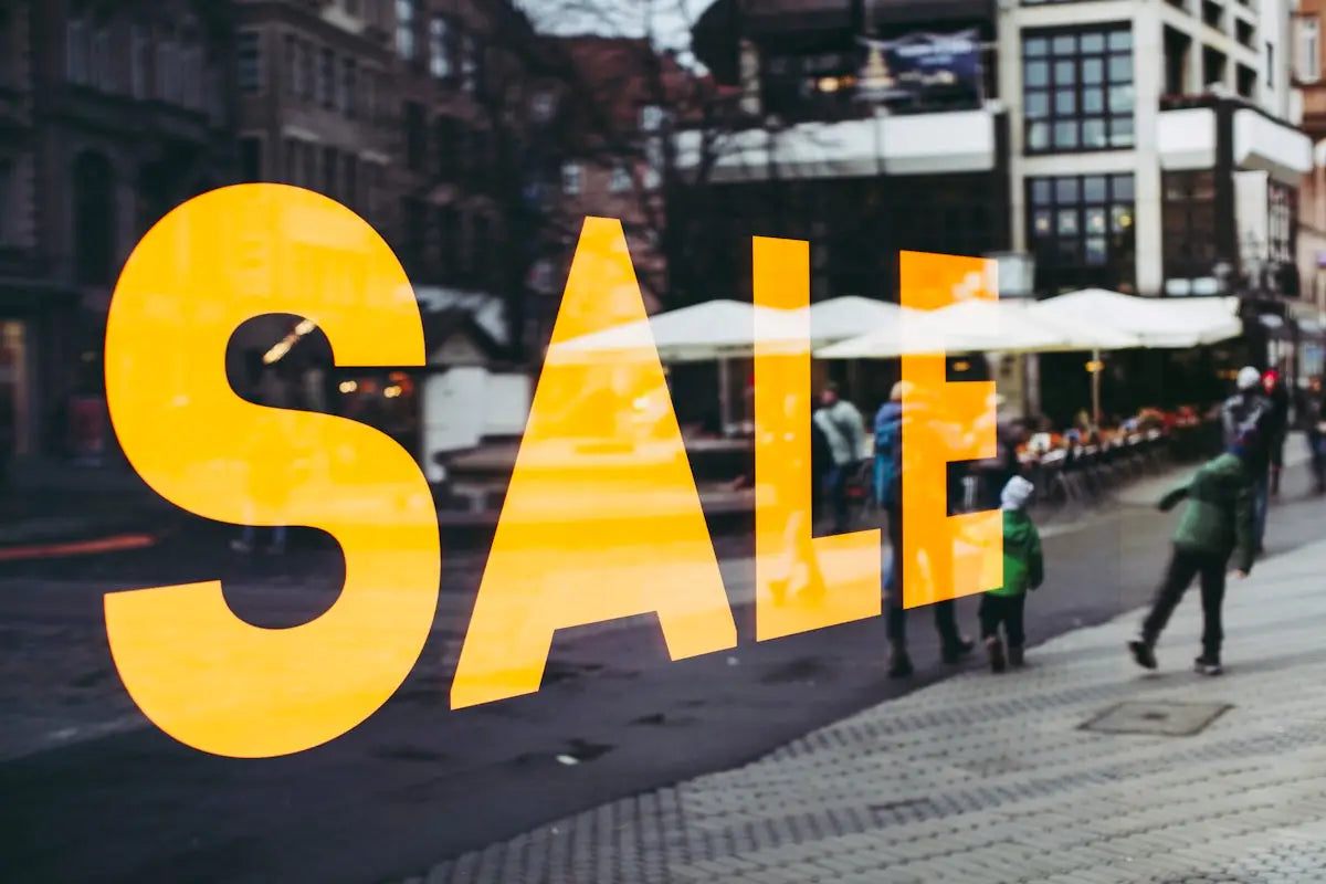 Bright yellow sale lettering prominently displayed on a storefront window for fashion and gadget savings.