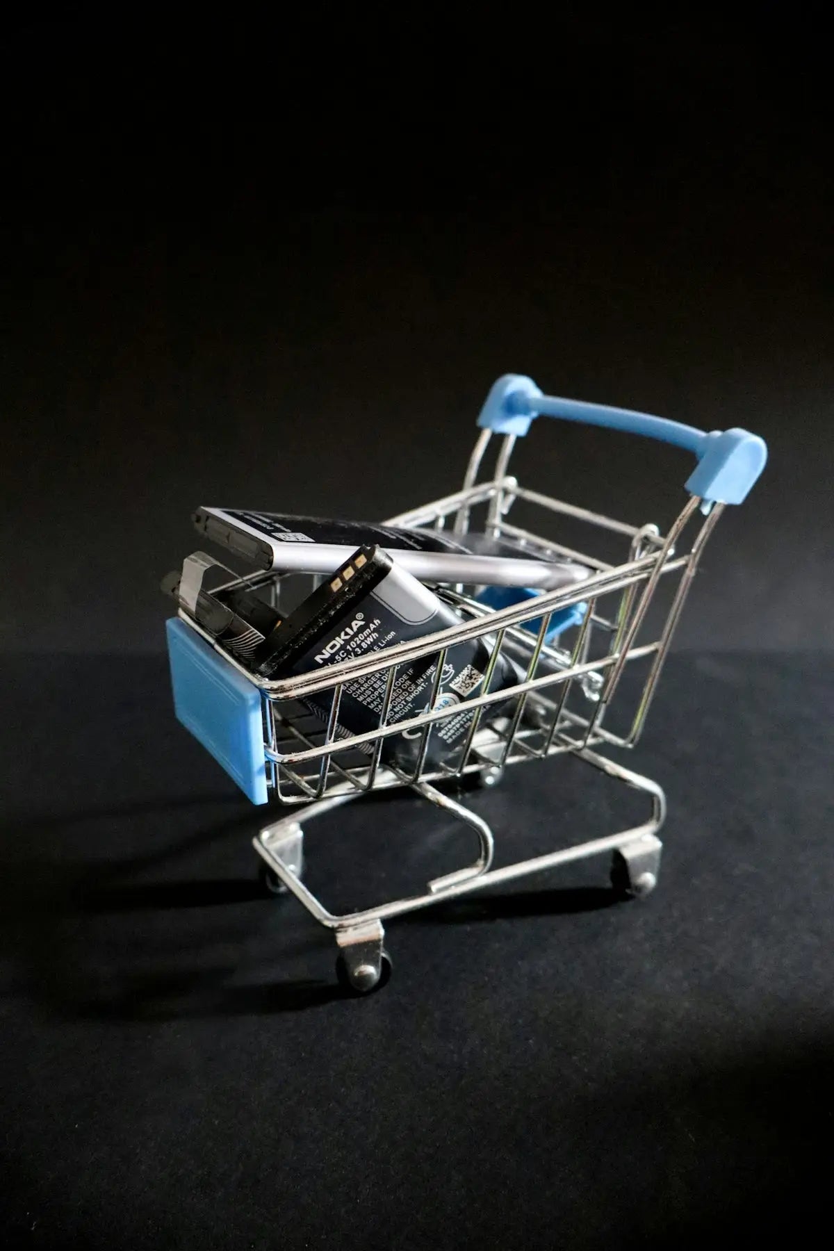 Miniature shopping cart with chrome frame and light blue handles carrying a nokia phone battery for trending products.