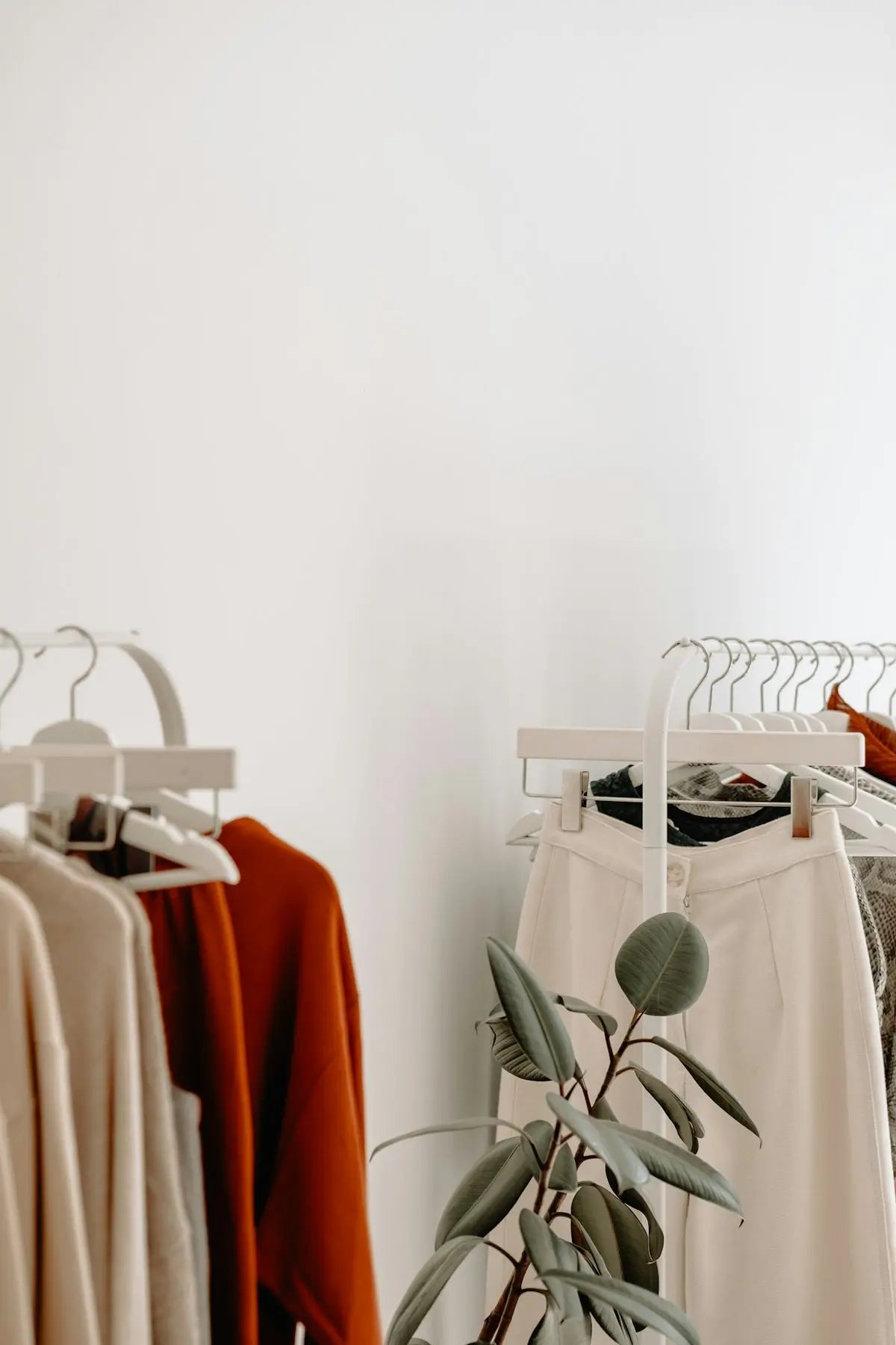 A sleek white minimalist clothing rack with modern design holds neatly arranged warm earthy tone garments for ecommerce fashion shopping.