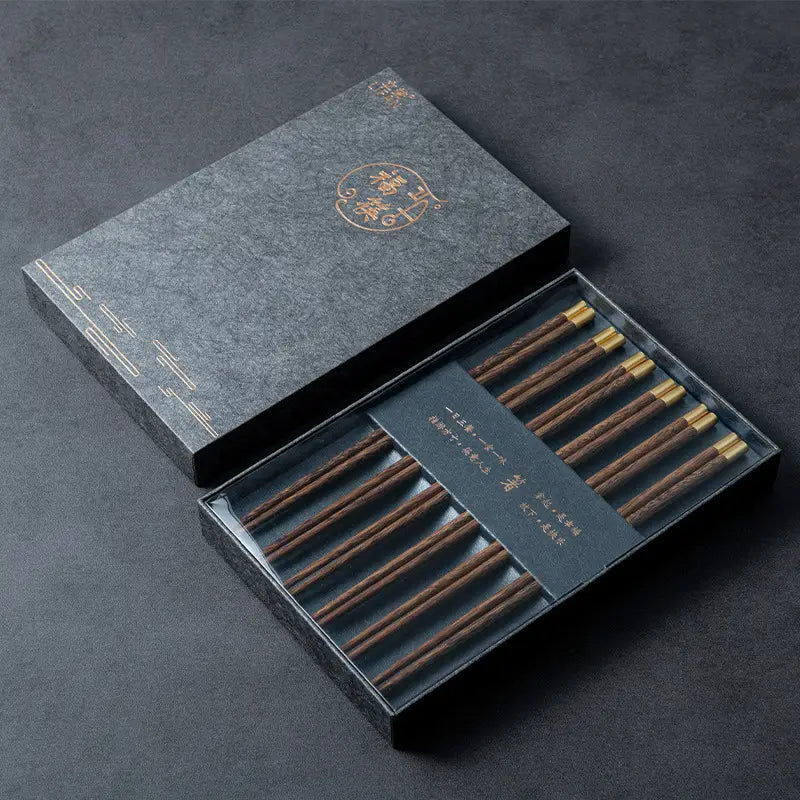 Set aus eleganten braunen hölzernen Essstäbchen mit goldfarbenen Spitzen, in einer anspruchsvollen dunkelgrauen Geschenkbox präsentiert, für ein Essstäbchen-Set mit goldfarbenen Spitzen, fünf Paar Geschenkbox.