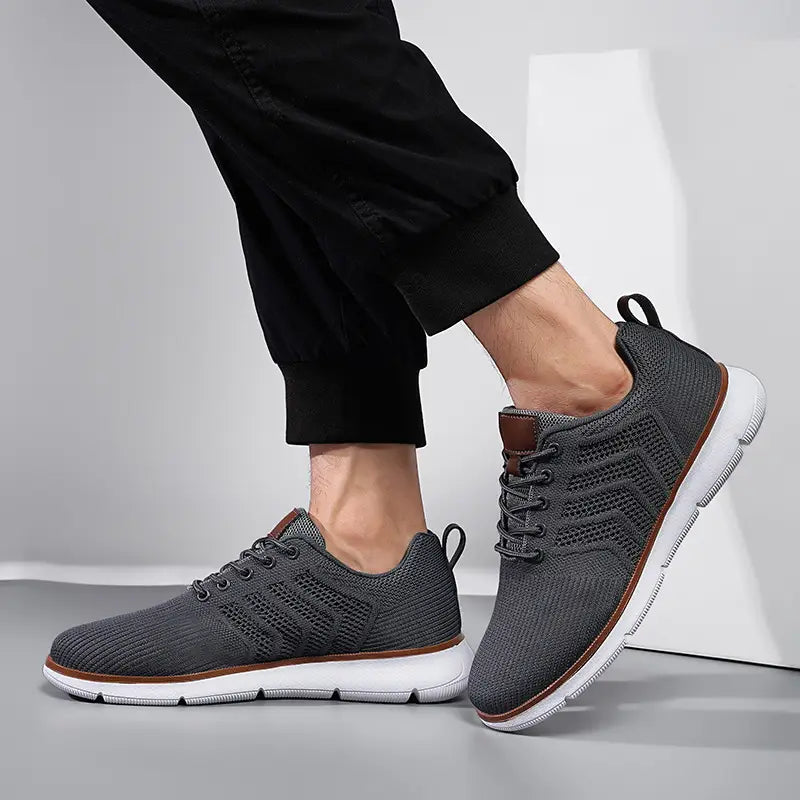 Gray mesh sneakers for men with brown leather accents and white soles designed as casual flying woven shoes.