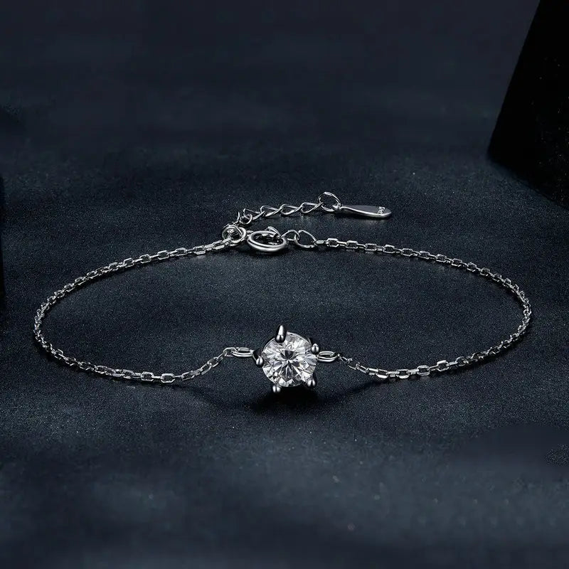 A delicate silver chain bracelet featuring a central round-cut clear moissanite gemstone held by four prongs.