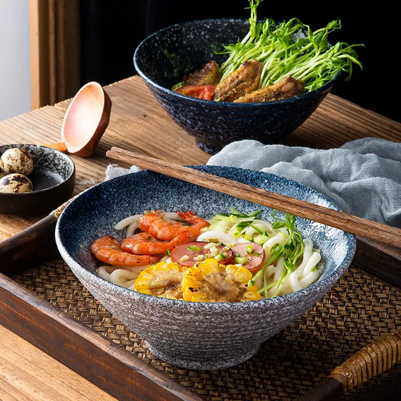 Eine gesprenkelte blaue Keramikschale aus einem Set „rustikale japanische Keramikschalen“ mit Tischgeschirr, gefüllt mit Udon-Nudeln, Garnelen und Gemüse.
