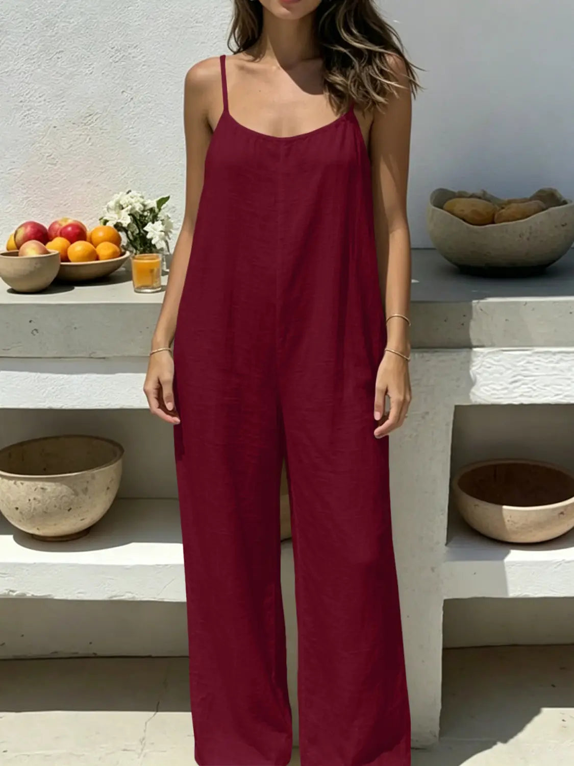 A flowing deep red linen wide leg backless sleeveless jumpsuit with thin spaghetti straps and wide-leg pants shown from the back.