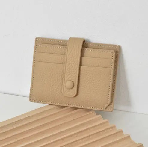 Beige ultra thin minimalist textured leather card holder with a button closure, stitched edges, and strap