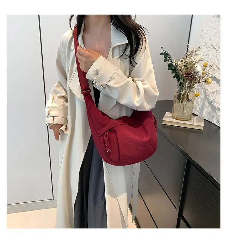 A vibrant red nylon crossbody bag with a large capacity and braided tassel detail designed as a lightweight hobo shoulder bag.