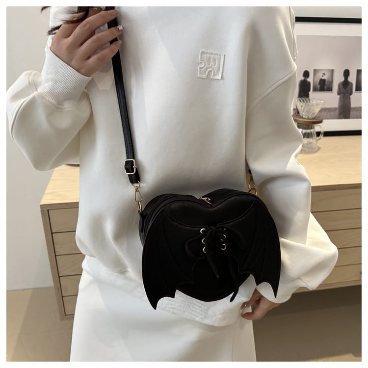 Black velvet bat-shaped crossbody bag with silver hardware and lace-up front detail called bat wing heart crossbody bag with lace up detail.