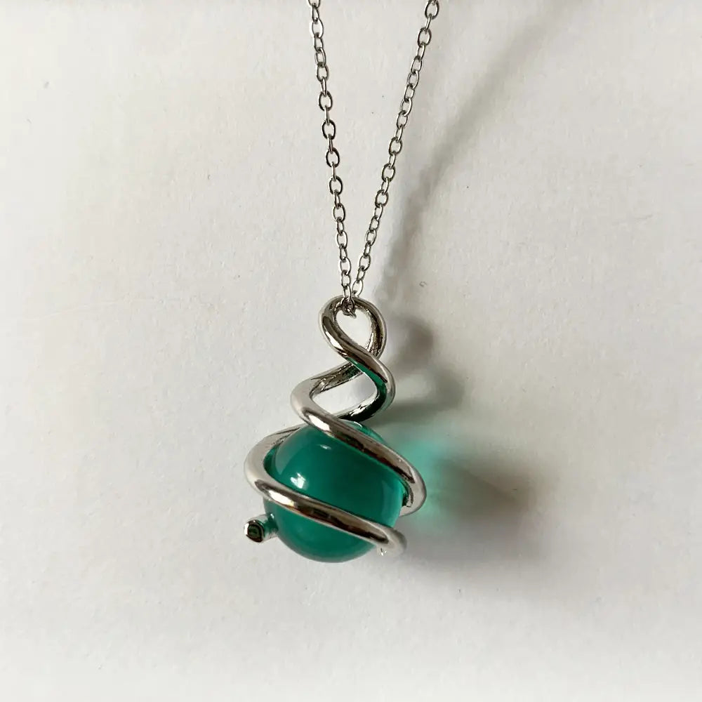 Collar de cadena de plata elegante y estilizado que presenta un colgante esférico de vidrio esmerilado verde vibrante, rodeado por una elegante espiral de alambre o metal retorcido.