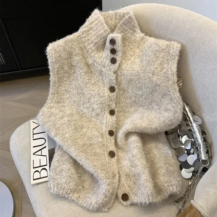 Un gilet en maille crème, confortable, à col haut et à boutons brun foncé, réalisé à partir d’un tissu en maille souple.
