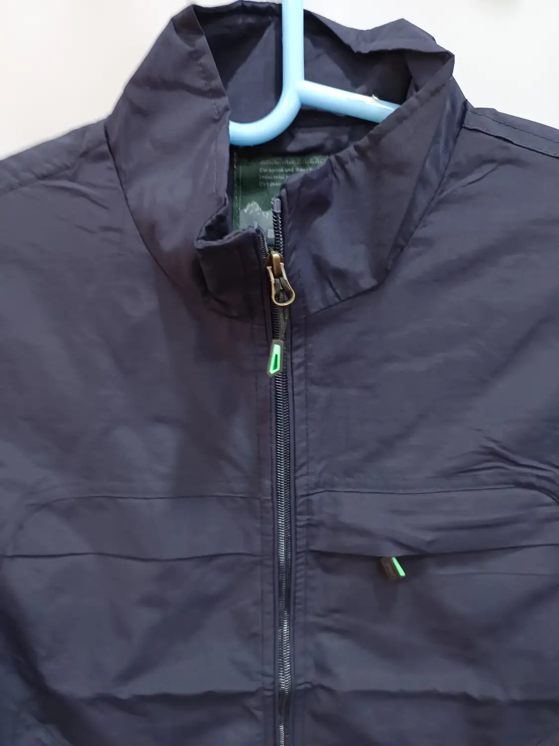 Chaleco utilitario impermeable de color azul marino oscuro con múltiples bolsillos, fabricado en nailon, con cuello alto y tiradores verdes de la cremallera.