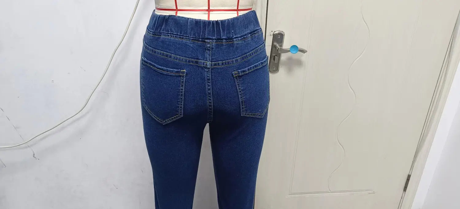The back side of high waist slim denim leggings in blue denim featuring a high-waisted elasticated waistband and two back pockets.