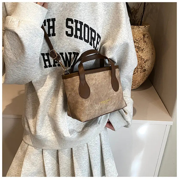 A beige textured mini retro bucket bag made of canvas with brown leather handles and an adjustable shoulder strap.