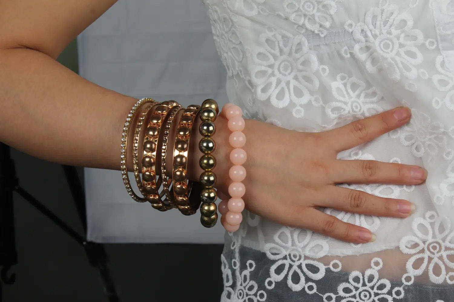 A stack of retro gold and pink rhinestone bangle bracelets featuring gold-toned and rose quartz beads worn on a wrist.