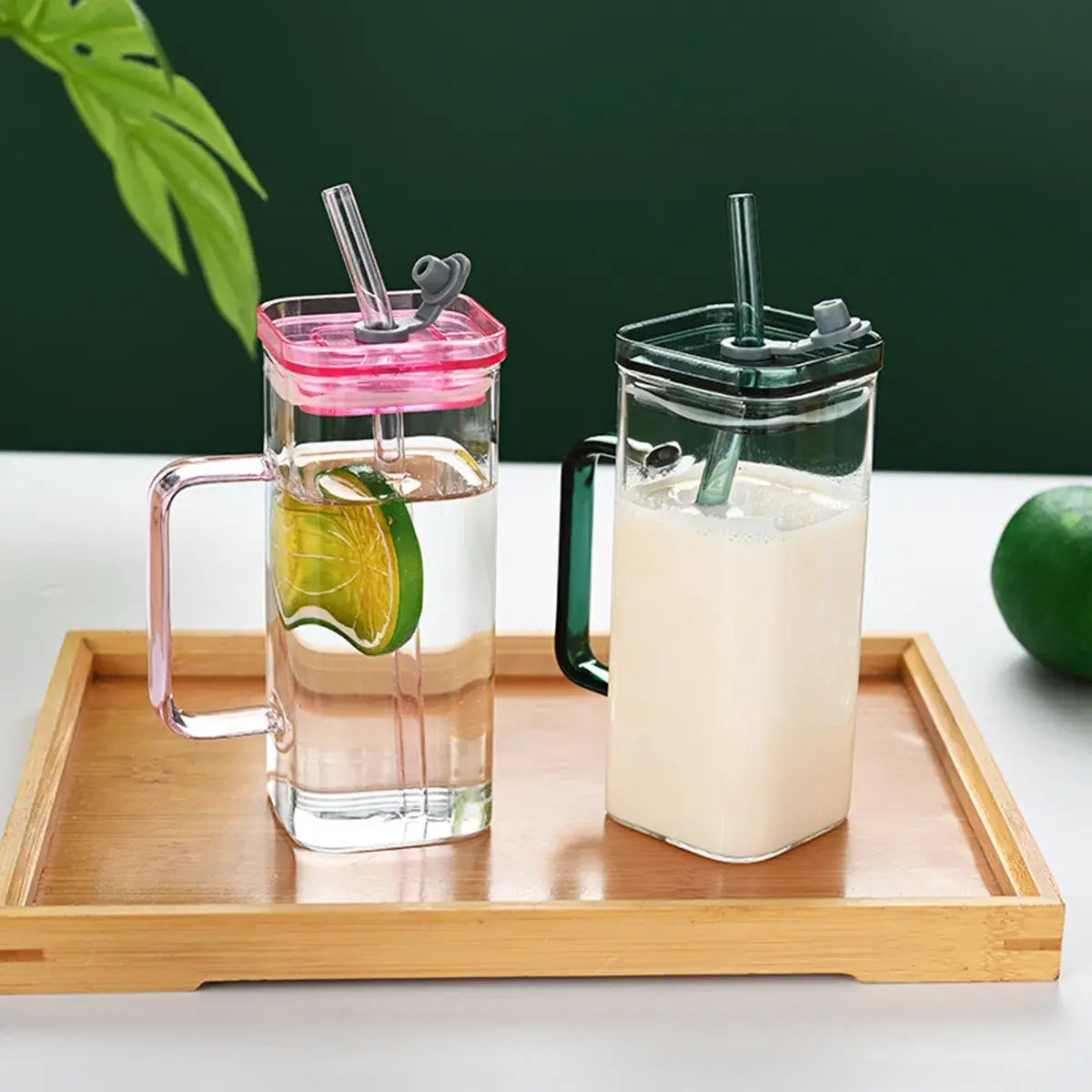 Deux carafes en verre transparent avec poignées, l’une avec un couvercle rose et l’autre avec un couvercle noir, chacune dotée d’un mécanisme à clapet et d’une paille, issues de la gamme de tasses carrées en verre avec couvercle et paille de 12 oz.