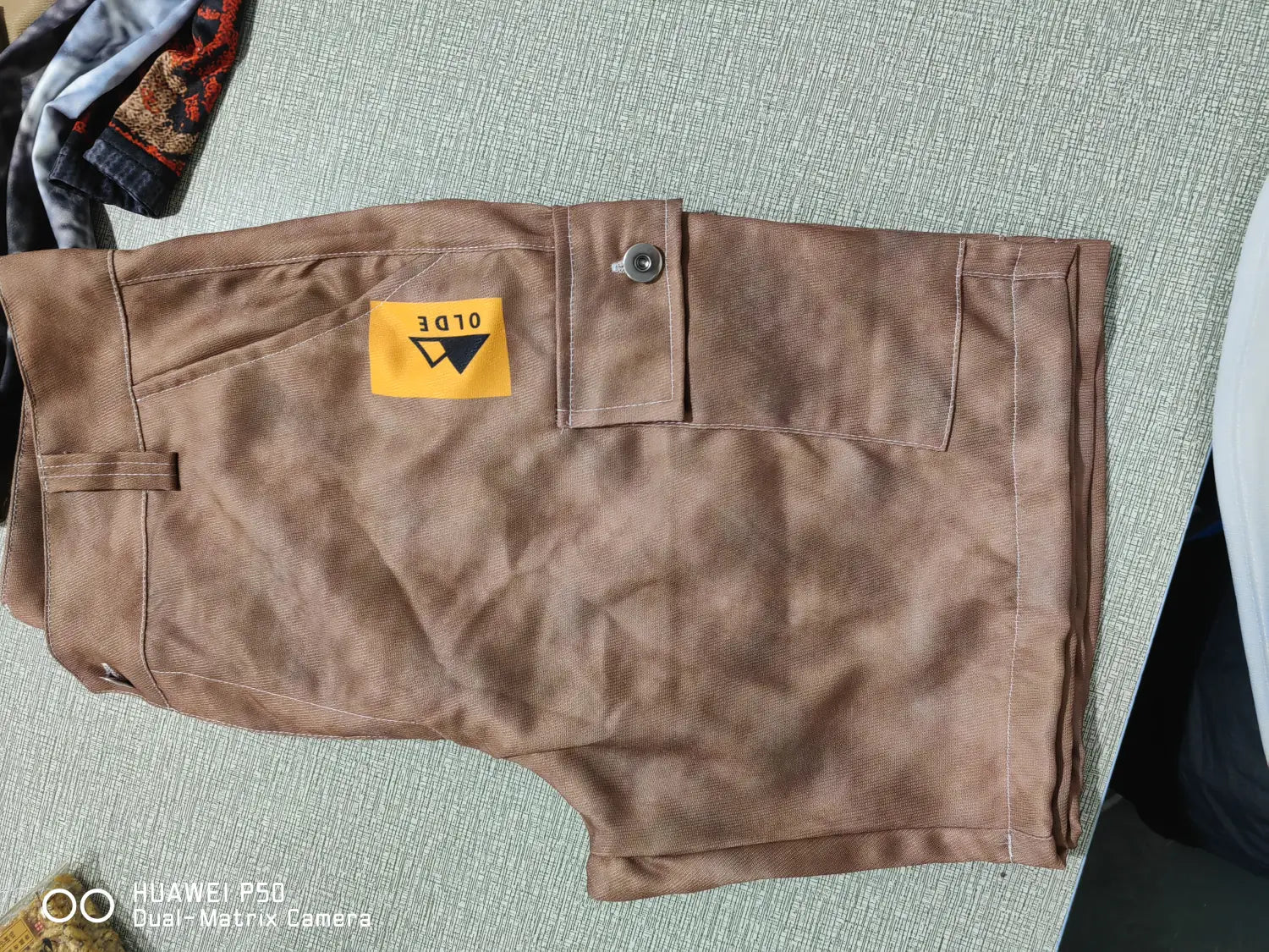 Men’s digital print cargo shorts in brown canvas polyester featuring a yellow label with old 3 text and a black triangle logo on the front right pocket.