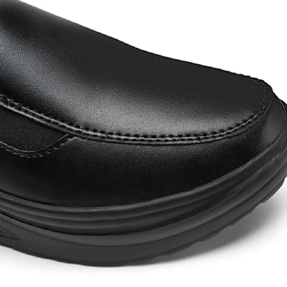 Chaussure slip-on à talon compensé en forme de coin en cuir noir, avec semelle en caoutchouc épaisse et superposée, présentée depuis l’arrière
