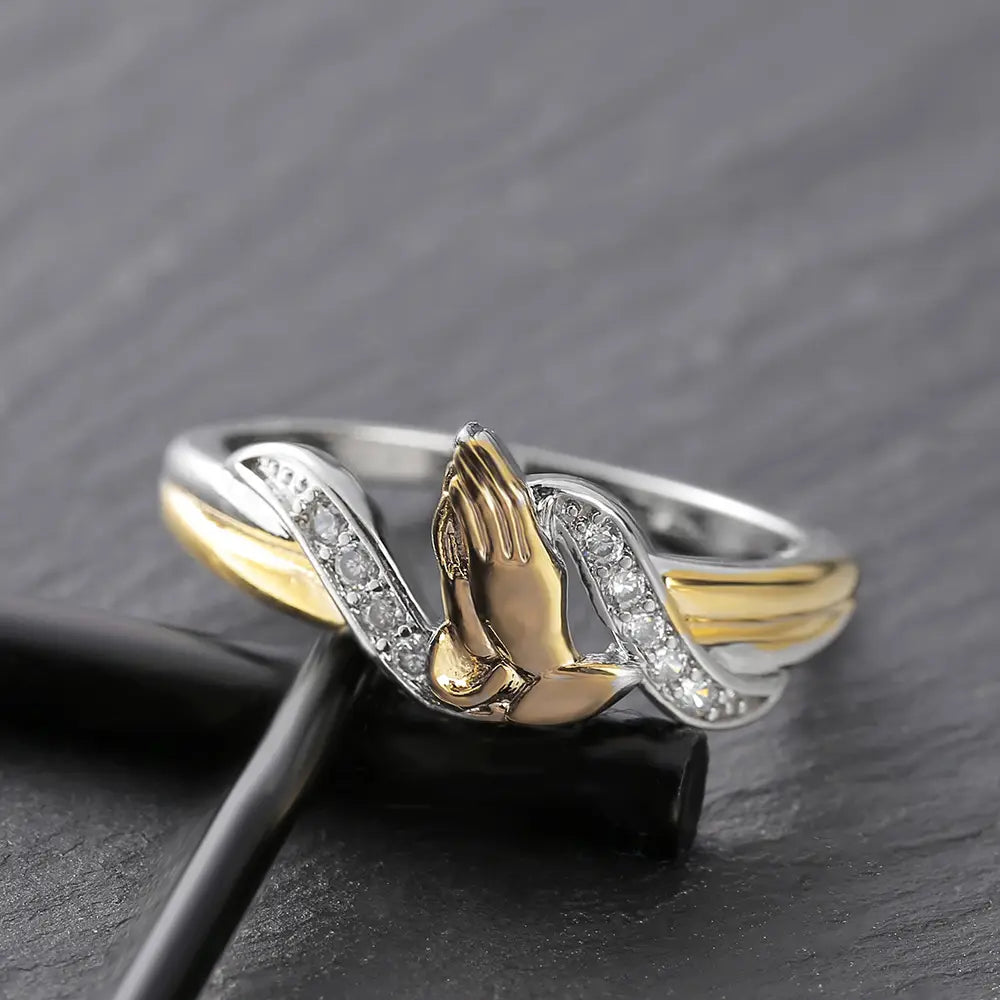 Two tone 18k gold and silver praying hands ring with detailed design and cubic zirconia stones embedded along the band.