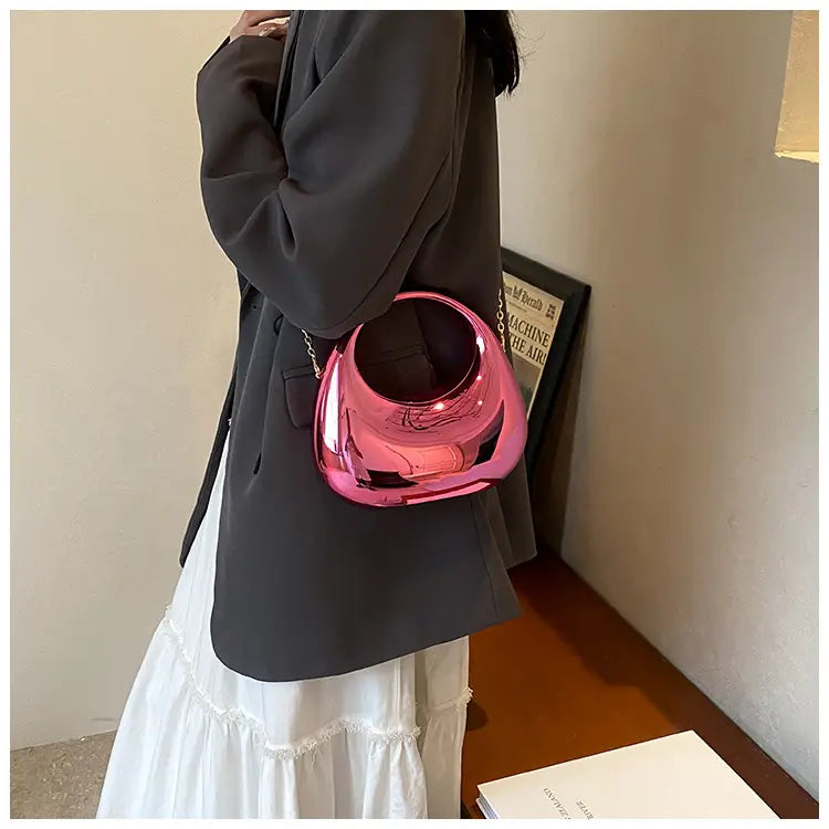 A glossy pink metallic acrylic clutch handbag with a unique rounded bowl-like shape and a gold chain strap.