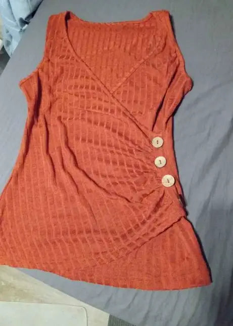 Camiseta tipo tank sin mangas con cuello en V y botón acanalado color naranja óxido, confeccionada en tejido de punto, con un patrón texturizado y tres botones de color claro en la parte delantera.