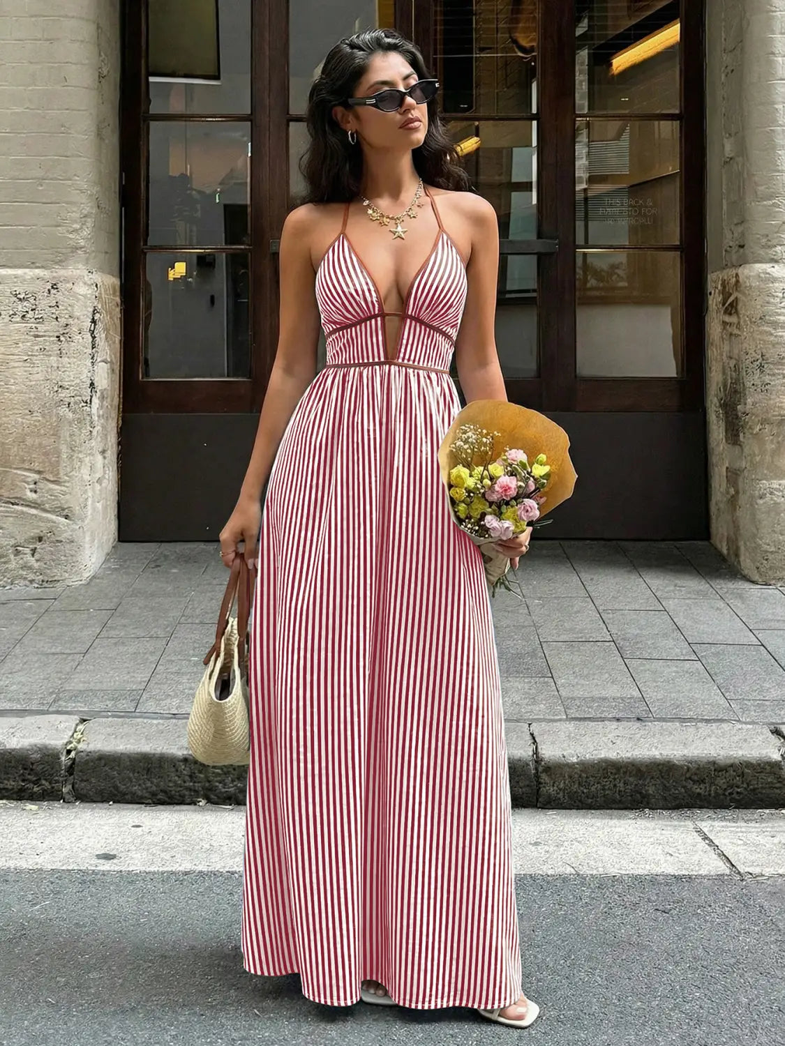Une robe maxi longue et fluide, montrée de dos, avec de larges rayures verticales roses et blanches, dotée d’une encolure en V et d’un design dos noué, adaptée pour l’été.