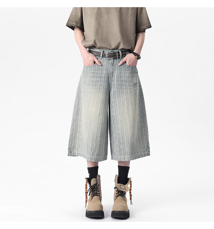 Striped denim capri shorts in light-wash denim featuring wide-leg cut, subtle vertical stripes, and a distressed patch on the thigh.