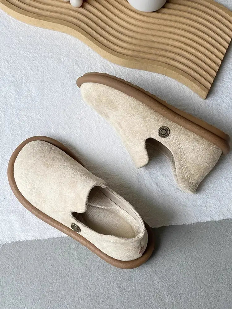 Beige Veloursleder-Slipper im Vintage-British-Stil mit niedrigem Absatz mit braun wirkenden Gummisohlen und dezenten metallisch wirkenden Knopfakzenten.