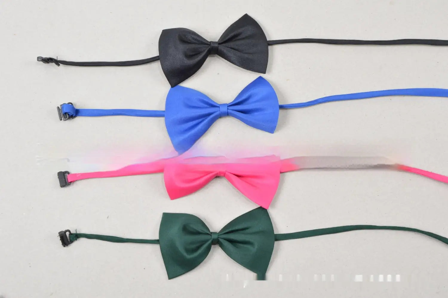 Se muestran cuatro collares para mascotas con lazos de color sólido ajustables en negro, azul, rosa y verde sobre una superficie lisa.