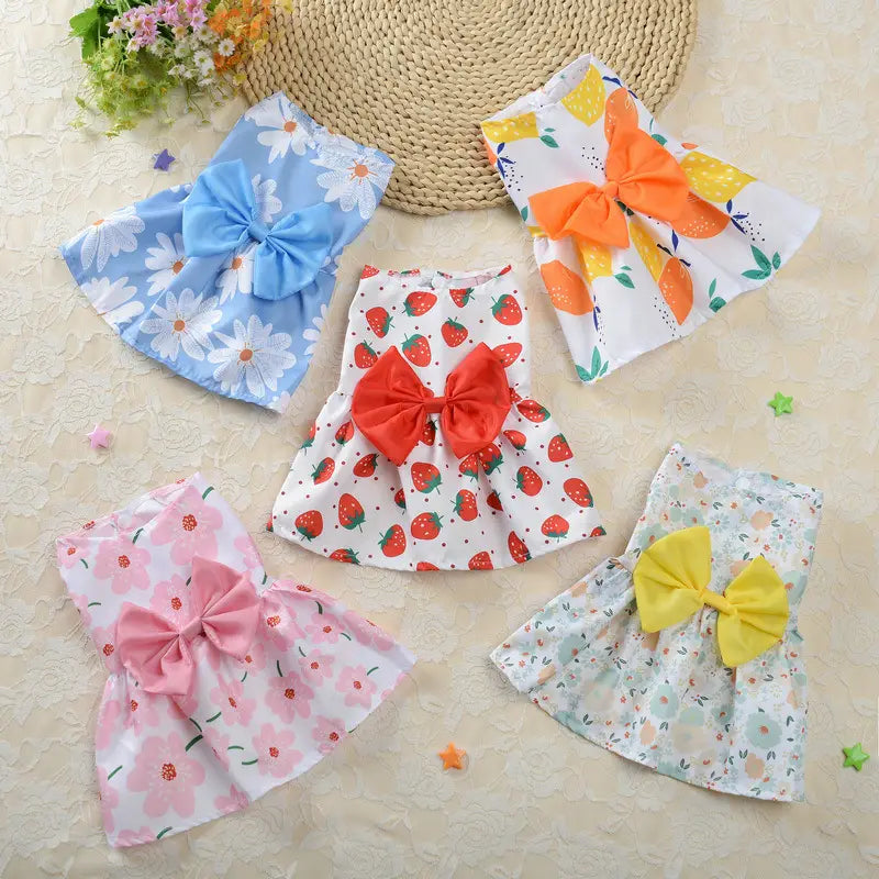 Four colorful floral dog princess dresses with large bow accents in blue red pink and yellow designed as strawberry daisy pet apparel.