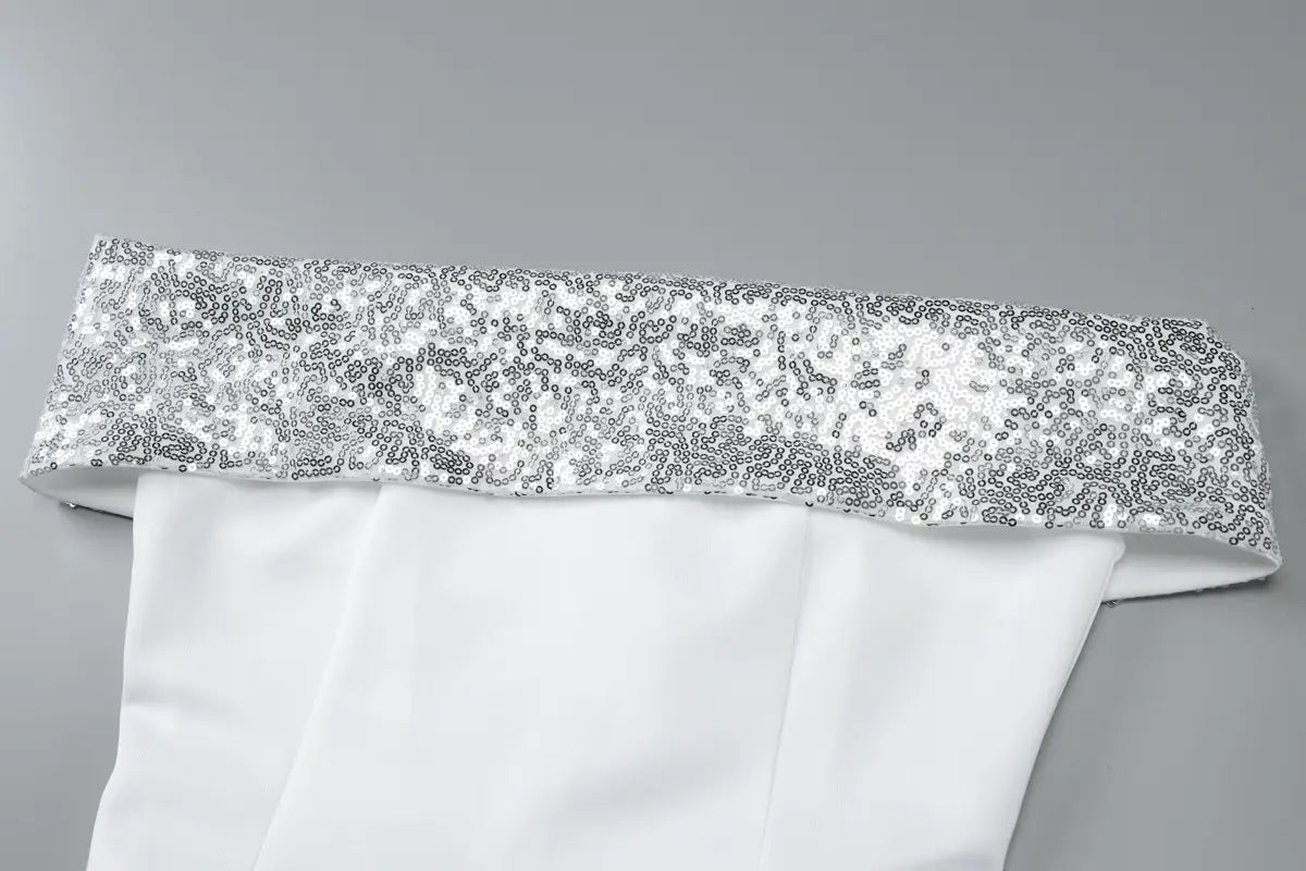 a sequined off-the-shoulder white bodycon mini dress featuring a shimmering silver sequined band along the top edge of the white fabric garment