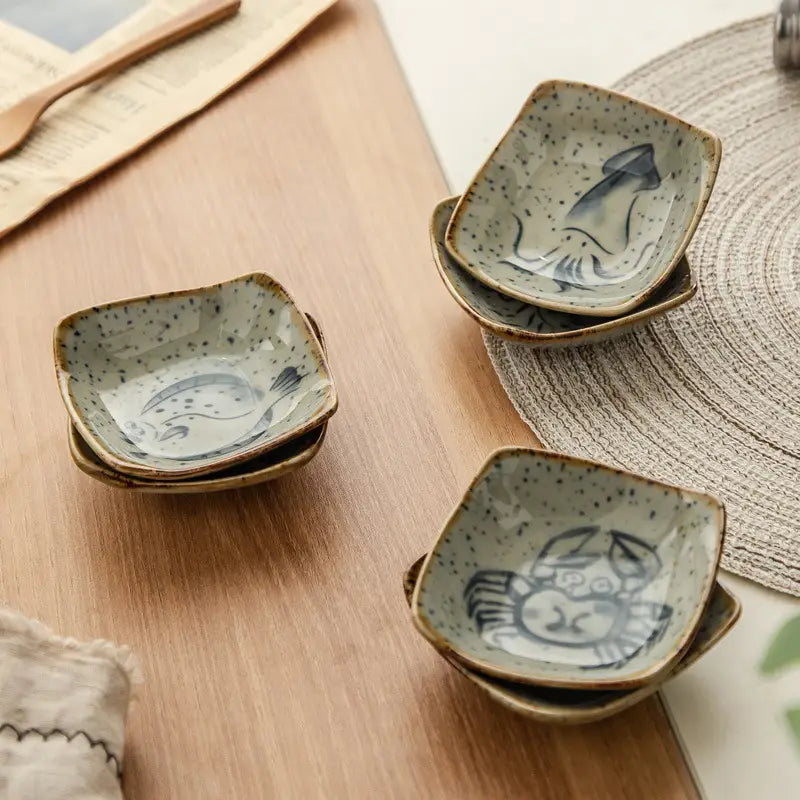 Handcrafted Japanese style ceramic sea creature sauce dish set featuring speckled beige glaze and hand-painted blue marine motifs.