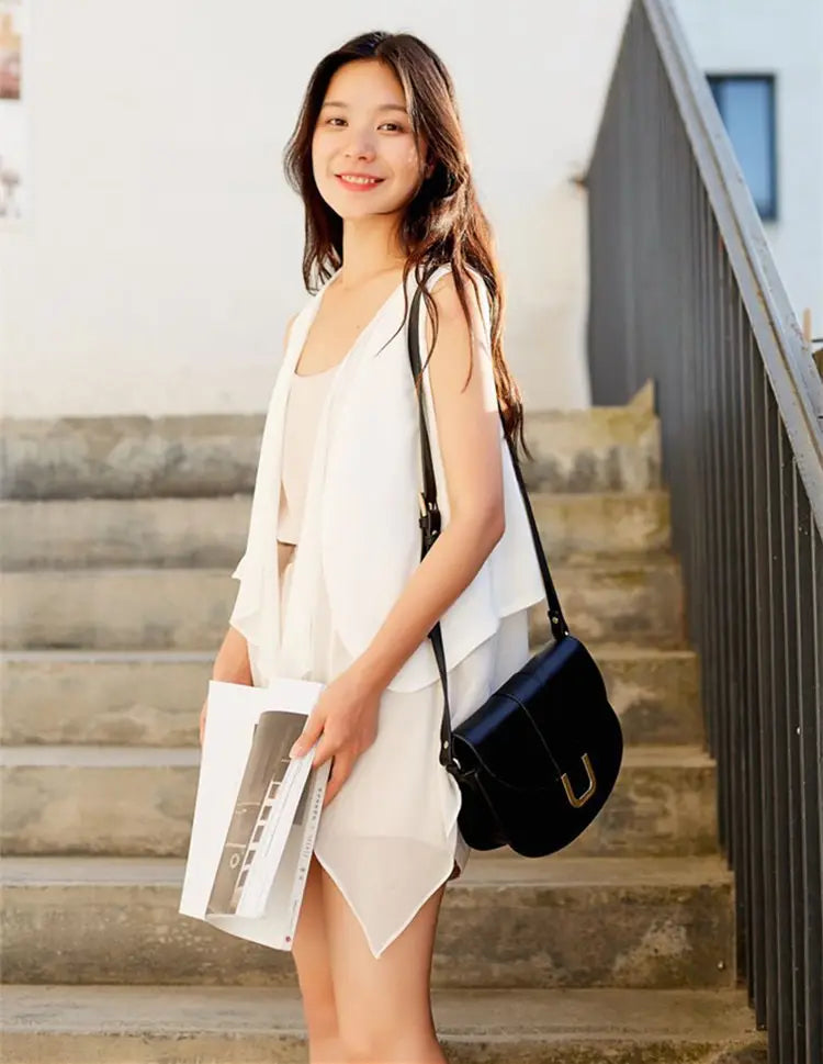 Schwarze Ledertasche im Satchel-Stil mit goldfarbenem U-förmigem Verschluss, kombiniert mit einem Chiffon-Lagenrock mit asymmetrischer Passform in einem stilvollen Ensemble