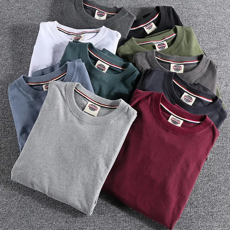Colección de camisetas tipo jersey de color liso lavado con cuello redondo y manga larga, dobladas con esmero, en blanco, gris, negro, verde oliva, burdeos y azul.