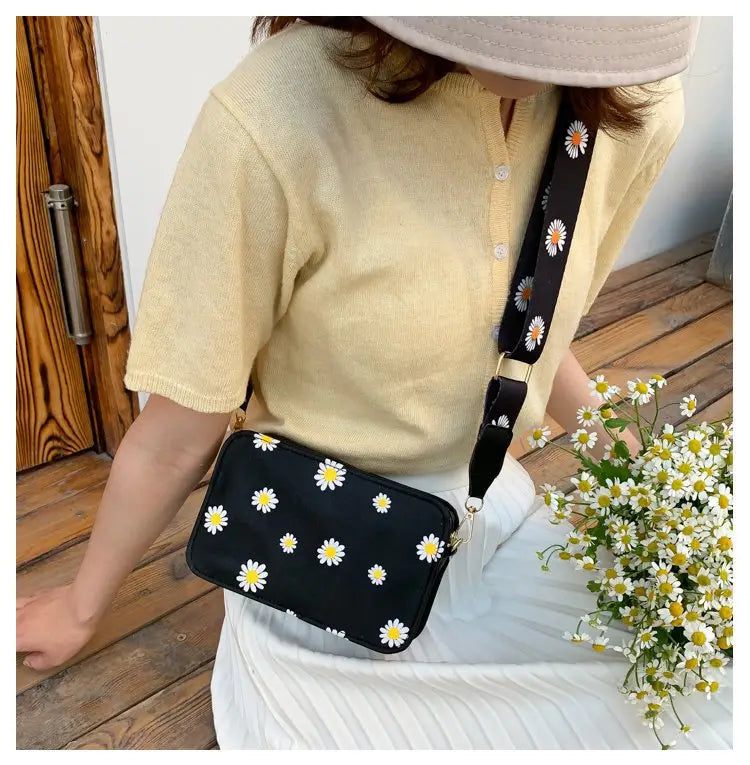 Black crossbody bag made of pu leather with white daisy prints and a matching chain strap.