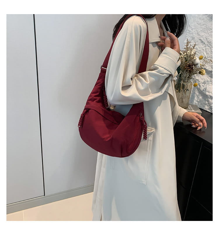 A sleek deep red nylon crossbody bag with large capacity hobo style and braided rope detailing on the shoulder straps and zipper pulls.