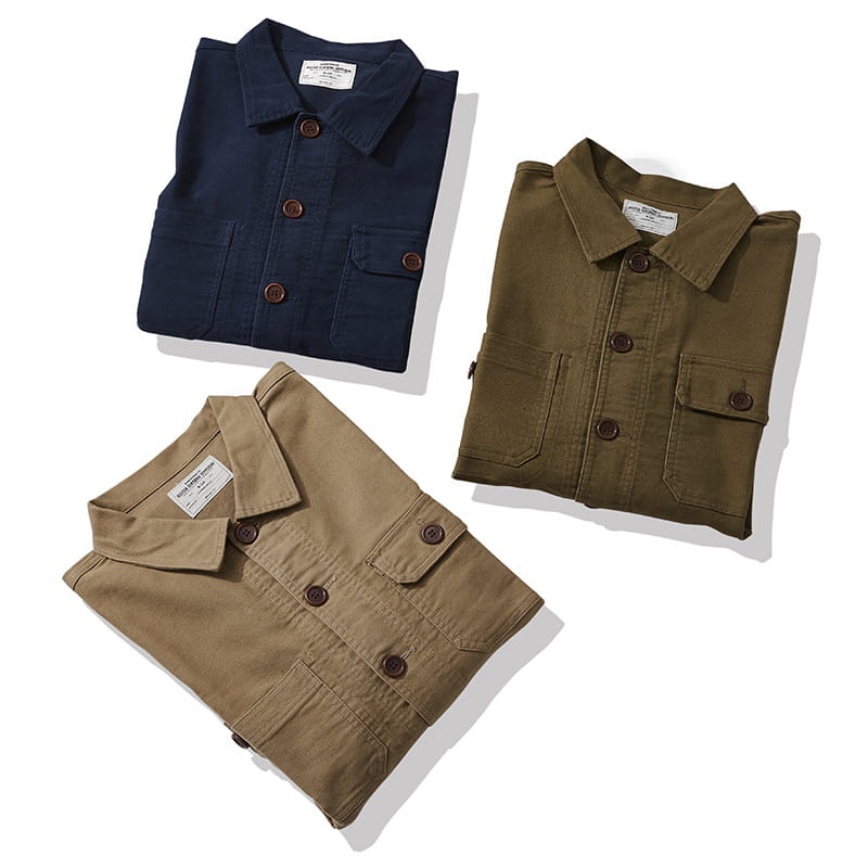 Three neatly folded mens french workwear jacket cotton utility pocket coats in navy blue olive green and khaki beige with brown wooden buttons.