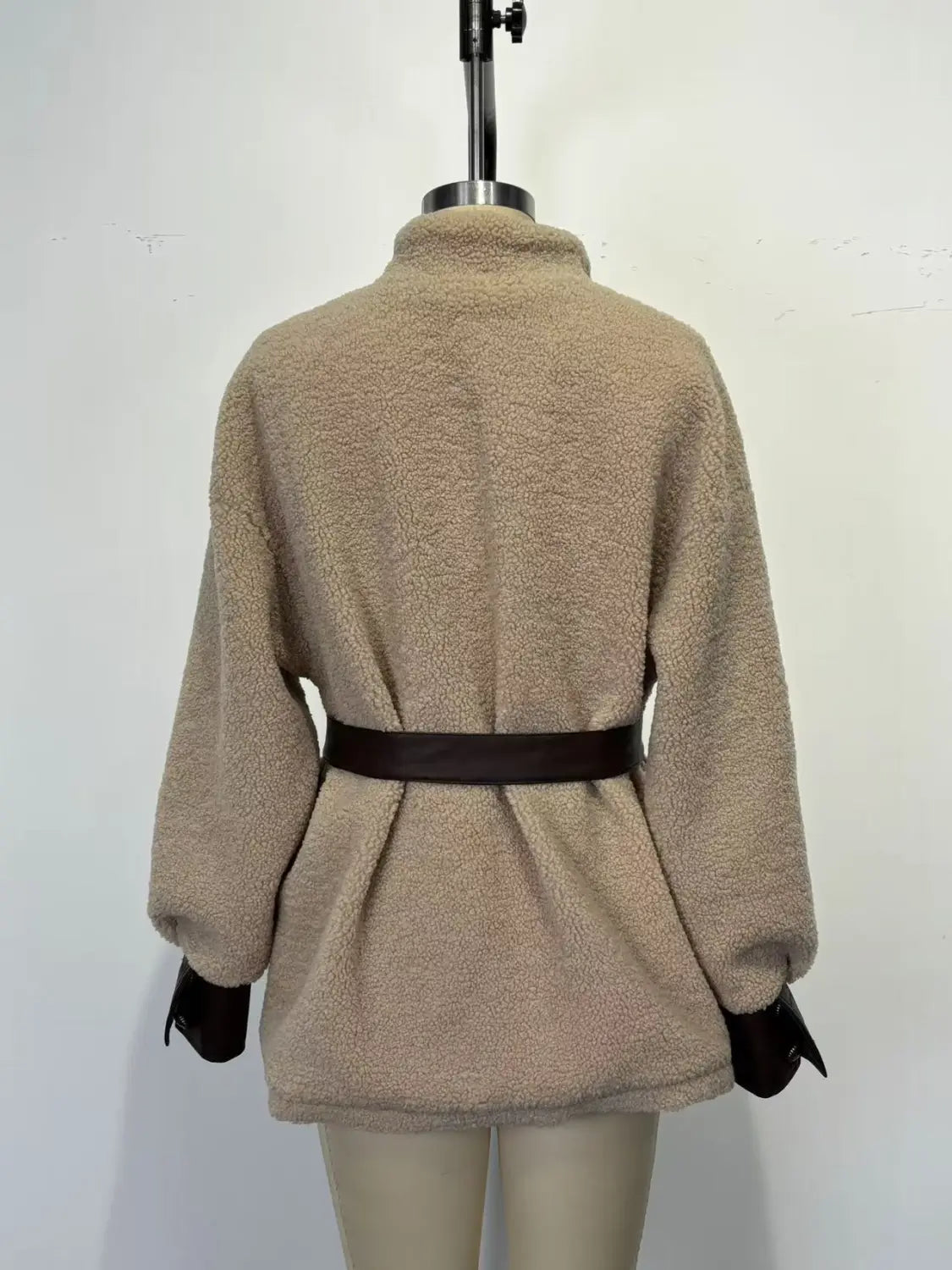 Beiger Shearling-Besatz-PU-Leder-Mantel mit Taillengürtel, mit hohem Kragen, langen Ärmeln und einem dunkelbraunen Gürtel, der die Taille betont.