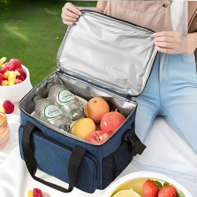insulated lunch bag large portable crossbody case in blue with black handles and silver-lined interior filled with fruit and bottled water