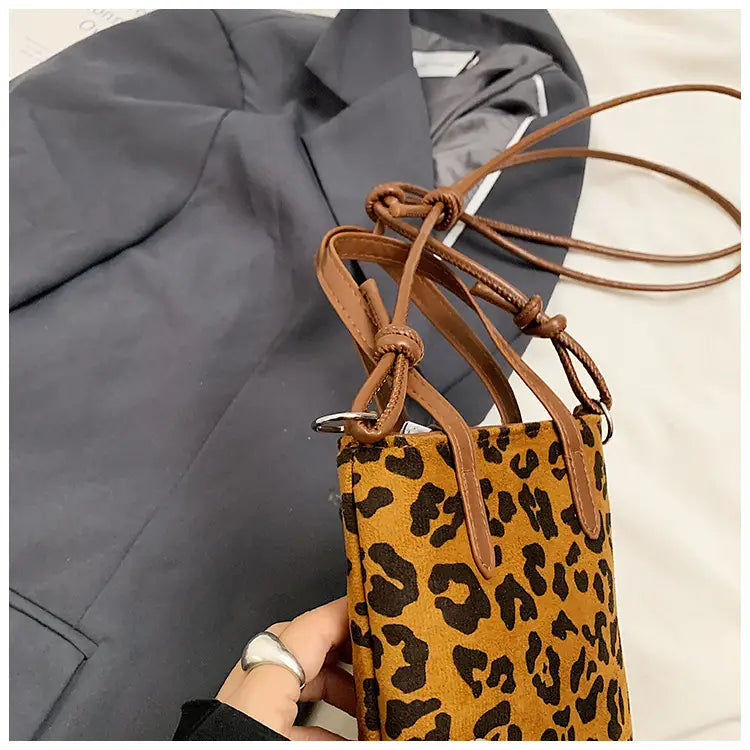 A tan and black leopard-print suede mini bucket crossbody bag with brown leather straps and handles.