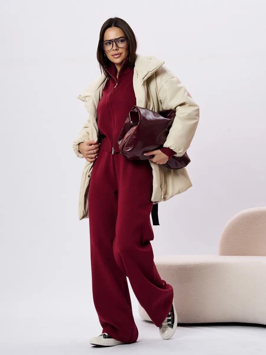 A plush deep burgundy leather handbag with a structured yet relaxed silhouette styled with a women’s knit zip up cardigan and wide leg pant set.