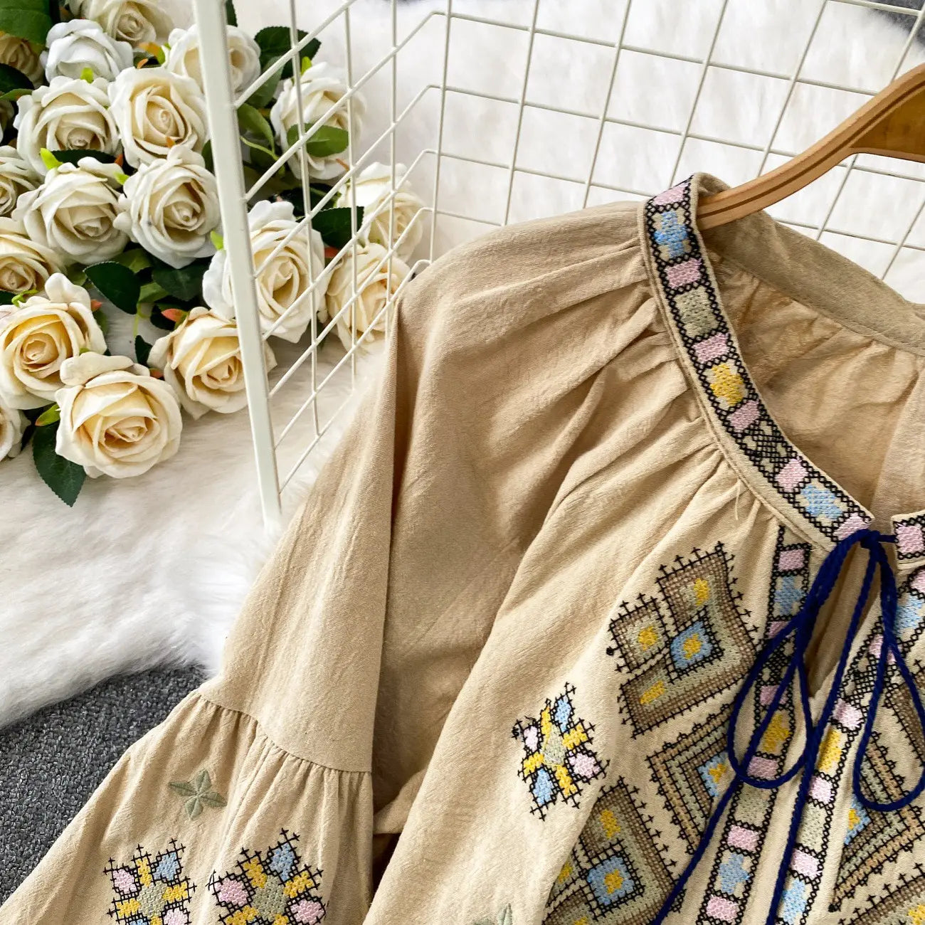 Beige embroidered lantern sleeve tie neck blouse with colorful geometric patterns and a blue tie at the neckline.