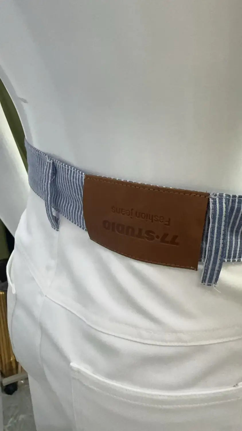 Ceinture rayée bleu et blanc avec languette en cuir brun portant le nom de la marque 77-studio, associée à un jean à taille avec bande blanche et jambes évasées