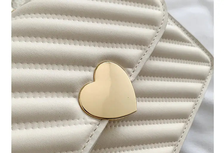 A cream-colored quilted crossbody bag made of soft material with a ruched handle and a gold heart-shaped clasp.