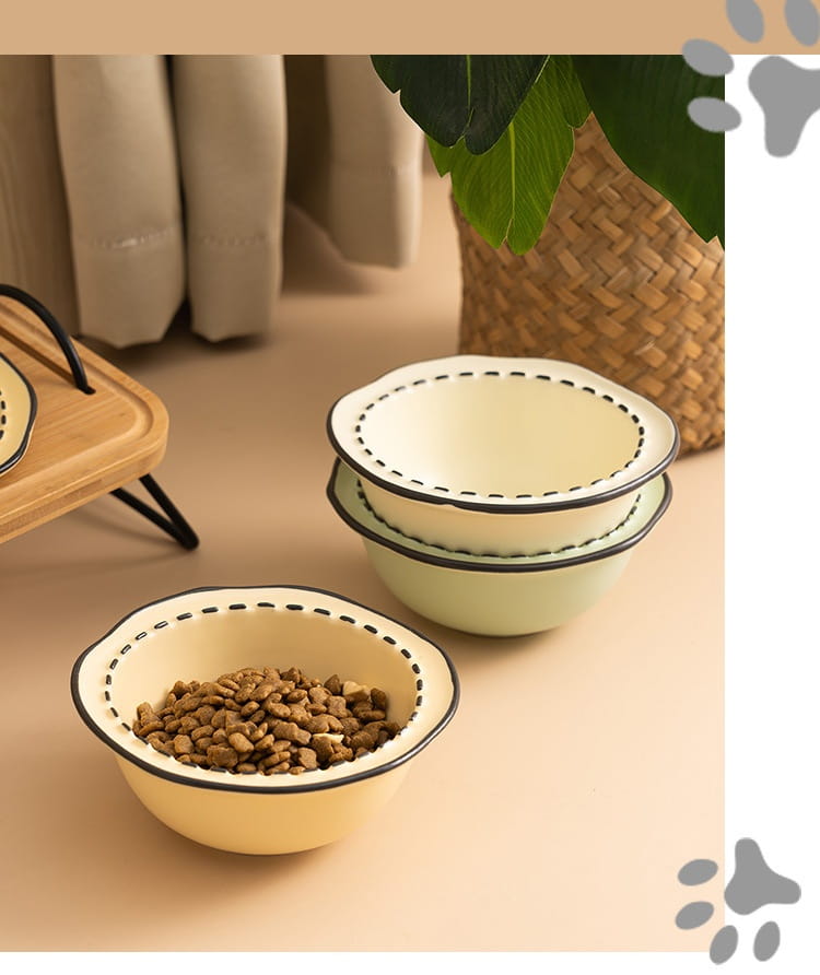 Cream-colored ceramic cat bowls with black dashed trim and scalloped edges in an elevated wooden stand.