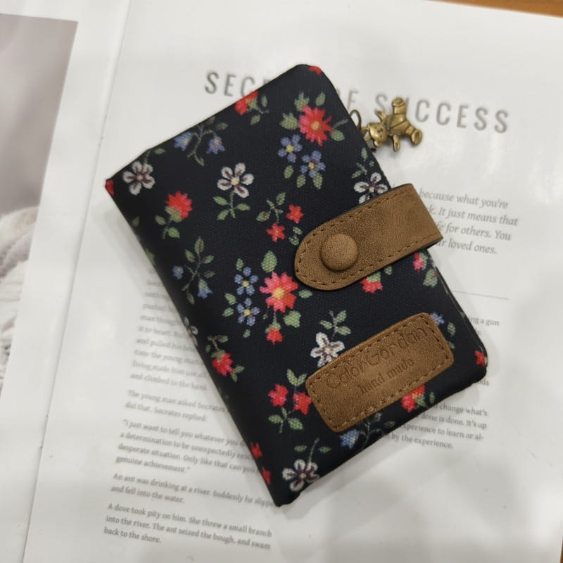 Whimsical patterned canvas tri fold multi card wallet with black floral pattern brown leather accents and small brass keychain.