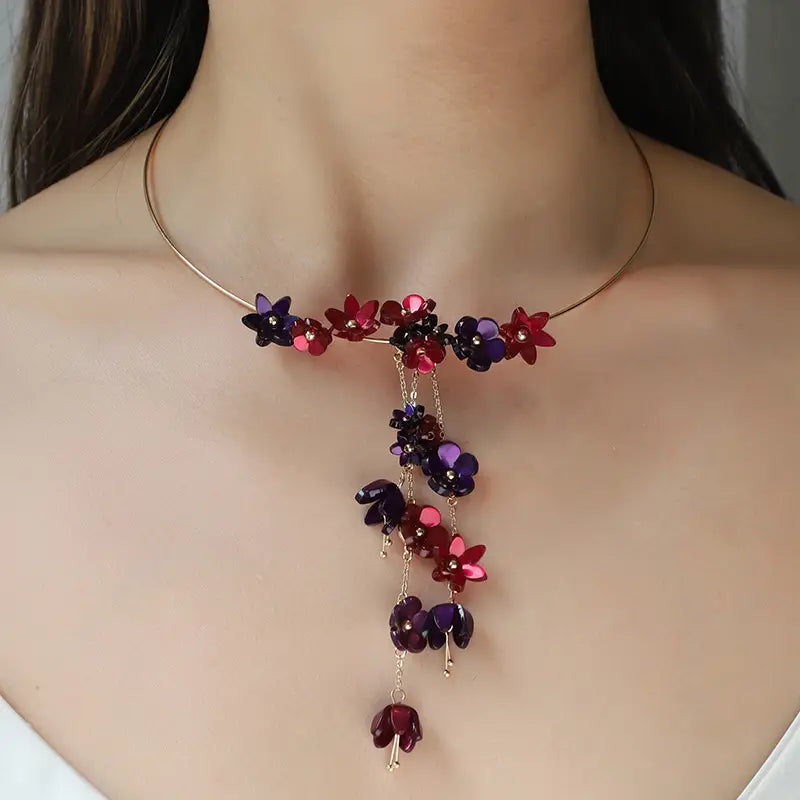 A gold layered choker necklace featuring delicate gold-toned metal with cascading clusters of vibrant red and deep purple acrylic floral charms.