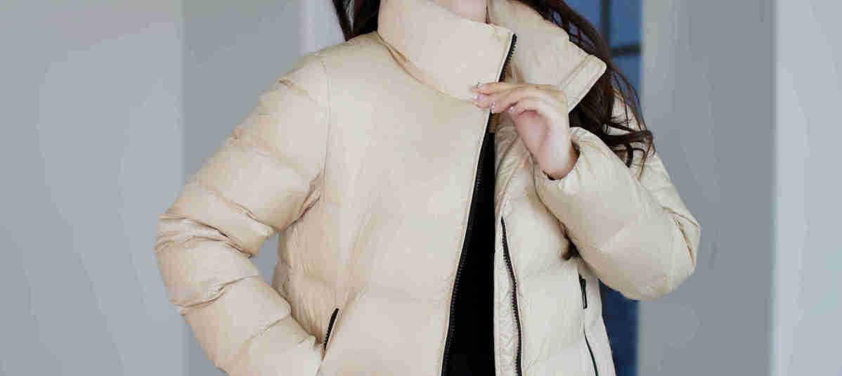 Beige kurze Steppjacke aus Daunen für Damen mit hohem Kragen und schwarzen Reißverschlussakzenten, ausgelegt für Winterbekleidung.