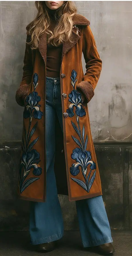 Ein Damen-Langmantel aus Wolle in rostfarbenem Veloursleder mit plüschigem braunem Shearling-Kragen sowie blauen Irisstickereien entlang der Vorderblenden.