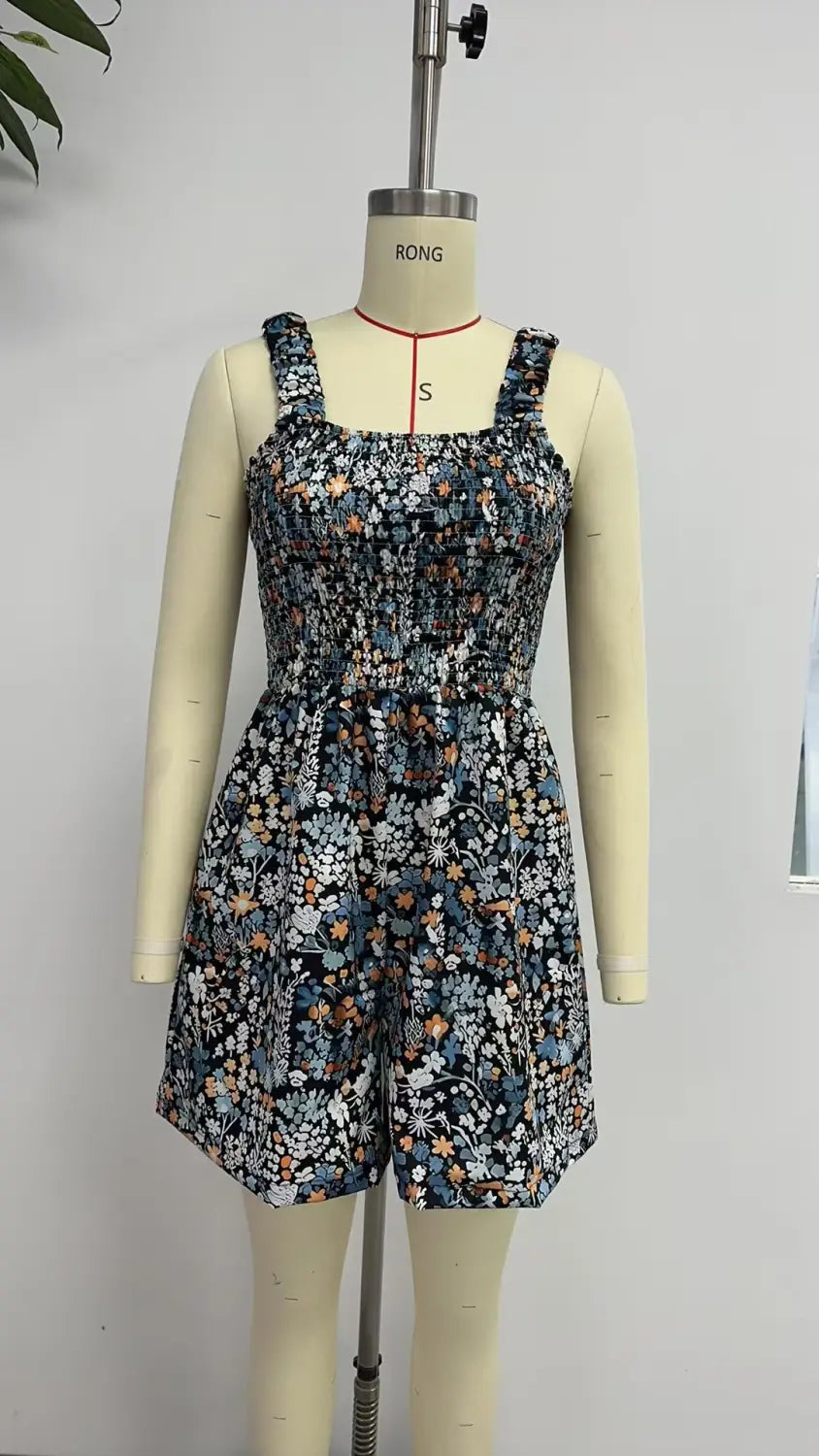 Mono de playa de verano sin mangas con estampado floral azul marino, tirantes finos y cintura fruncida, presentado en un maniquí.