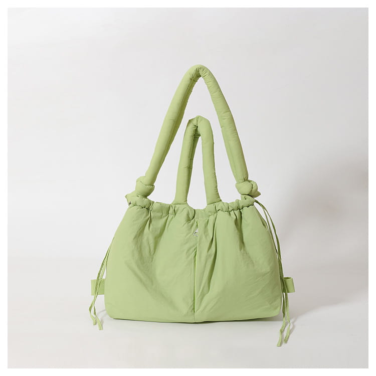 A soft light green quilted puffer tote bag made of lightweight nylon with thick knotted handles and drawstring ties designed for shoulder use.
